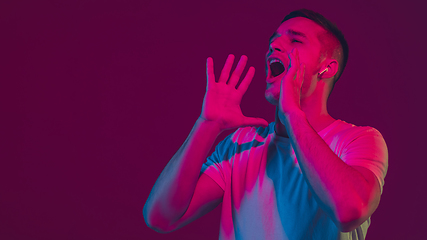 Image showing Caucasian man\'s portrait isolated on pink-purple studio background in neon light, using wireless earphones