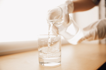 Image showing Close up of female hand holding bottle and glass, pouring pure water