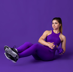 Image showing Beautiful young female athlete practicing on purple studio background, monochrome portrait