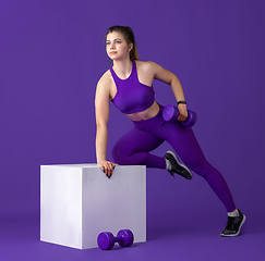 Image showing Beautiful young female athlete practicing on purple studio background, monochrome portrait