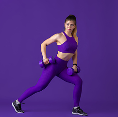 Image showing Beautiful young female athlete practicing on purple studio background, monochrome portrait