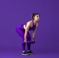 Image showing Beautiful young female athlete practicing on purple studio background, monochrome portrait