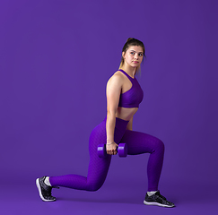 Image showing Beautiful young female athlete practicing on purple studio background, monochrome portrait