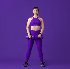 Image showing Beautiful young female athlete practicing on purple studio background, monochrome portrait