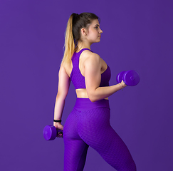 Image showing Beautiful young female athlete practicing on purple studio background, monochrome portrait