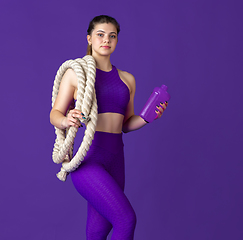 Image showing Beautiful young female athlete practicing on purple studio background, monochrome portrait