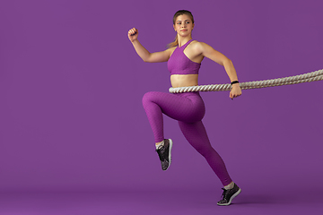 Image showing Beautiful young female athlete practicing on purple studio background, monochrome portrait