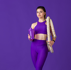 Image showing Beautiful young female athlete practicing on purple studio background, monochrome portrait