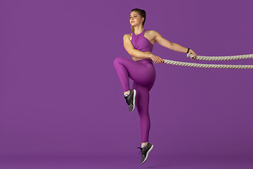 Image showing Beautiful young female athlete practicing on purple studio background, monochrome portrait