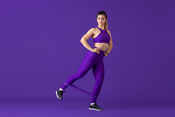 Image showing Beautiful young female athlete practicing on purple studio background, monochrome portrait