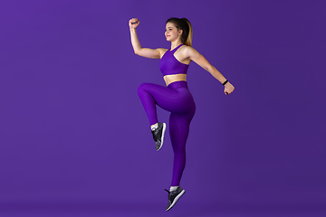 Image showing Beautiful young female athlete practicing on purple studio background, monochrome portrait