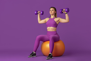 Image showing Beautiful young female athlete practicing on purple studio background, monochrome portrait