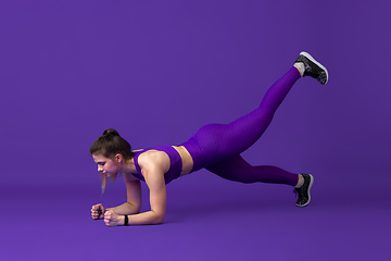 Image showing Beautiful young female athlete practicing on purple studio background, monochrome portrait