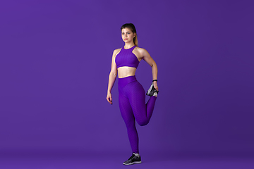 Image showing Beautiful young female athlete practicing on purple studio background, monochrome portrait