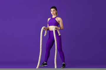 Image showing Beautiful young female athlete practicing on purple studio background, monochrome portrait