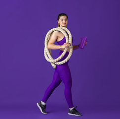 Image showing Beautiful young female athlete practicing on purple studio background, monochrome portrait