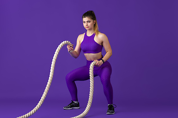 Image showing Beautiful young female athlete practicing on purple studio background, monochrome portrait