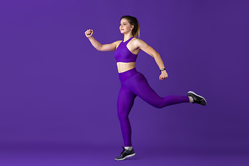 Image showing Beautiful young female athlete practicing on purple studio background, monochrome portrait