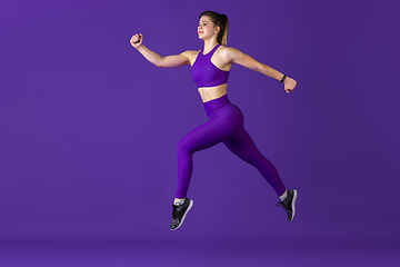 Image showing Beautiful young female athlete practicing on purple studio background, monochrome portrait