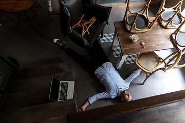 Image showing Public institutions closed due to COVID-19 or Coronavirus outbreak lockdown, stressed owner of small business alone lying down the floor in his cafe, restaurant, bar