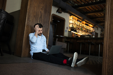 Image showing Public institutions closed due to COVID-19 or Coronavirus outbreak lockdown, stressed owner of small business alone lying down the floor in his cafe, restaurant, bar