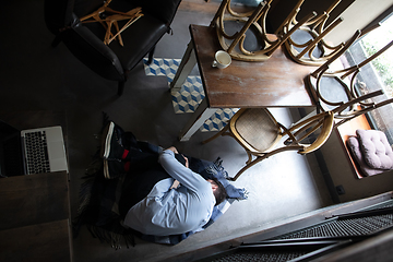 Image showing Public institutions closed due to COVID-19 or Coronavirus outbreak lockdown, stressed owner of small business alone lying down the floor in his cafe, restaurant, bar