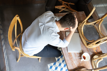 Image showing Public institutions closed due to COVID-19 or Coronavirus outbreak lockdown, stressed owner of small business alone in his cafe, looking for solution, top view