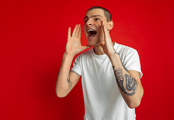 Image showing Caucasian young man\'s portrait on red studio background, emotinal and expressive