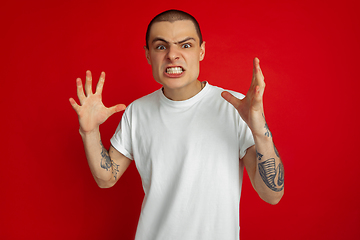 Image showing Caucasian young man\'s portrait on red studio background, emotinal and expressive