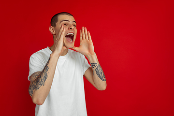 Image showing Caucasian young man\'s portrait on red studio background, emotinal and expressive