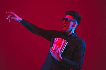 Image showing Caucasian man\'s portrait isolated on red studio background in purple-blue neon light, emotional and beautiful, looking throught 3D-eyewear, cinema