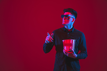 Image showing Caucasian man\'s portrait isolated on red studio background in purple-blue neon light, emotional and beautiful, looking throught 3D-eyewear, cinema