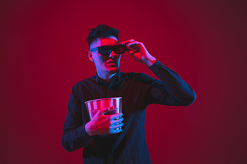 Image showing Caucasian man\'s portrait isolated on red studio background in purple-blue neon light, emotional and beautiful, looking throught 3D-eyewear, cinema