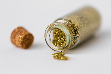 Image showing golden glitters poured from small glass bottle