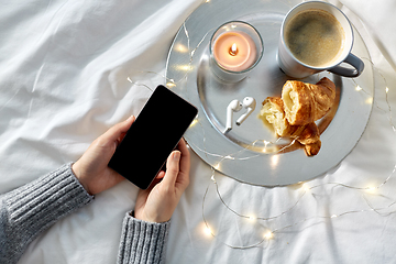 Image showing hands with smartphone, croissant and coffee in bed