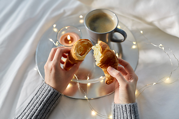 Image showing hands of woman eating croissant with coffee in bed