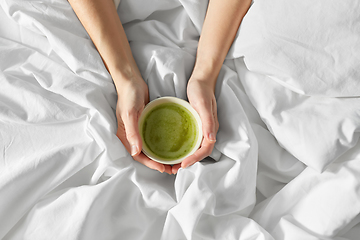 Image showing hands of woman with cup of matcha tea in bed