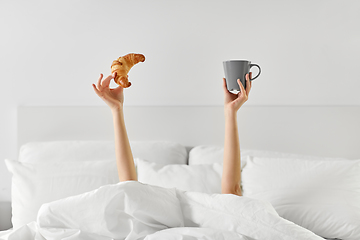 Image showing woman with coffee and croissant lying in bed