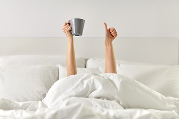 Image showing woman with coffee lying in bed showing thumbs up