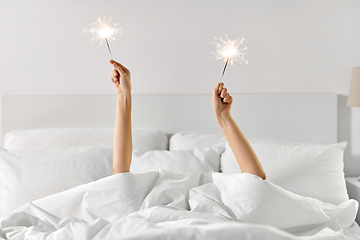 Image showing hands of woman lying in bed with sparklers