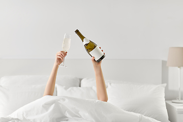 Image showing hands of woman lying in bed with champagne