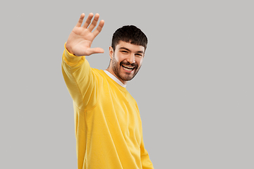 Image showing smiling young man in yellow sweatshirt waving hand