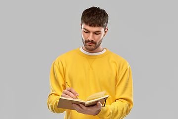 Image showing man in yellow sweatshirt writing to diary