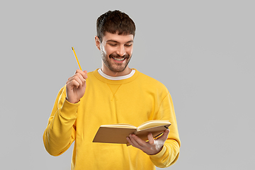 Image showing happy man in yellow sweater with diary and pencil