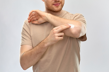 Image showing young man applying pain medication to his elbow