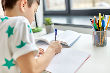 Image showing close up of boy writing to notebook at home