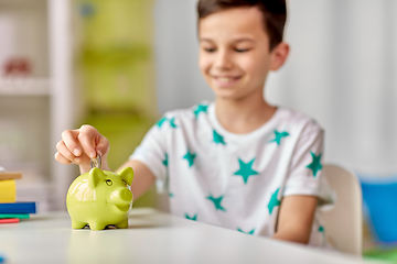 Image showing little boy putting coin into piggy bank at home