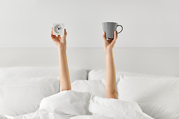 Image showing woman with coffee and alarm clock lying in bed