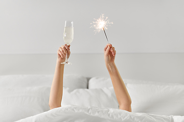 Image showing hands of woman in bed with champagne and sparkler