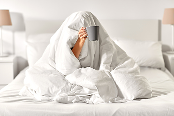 Image showing woman with coffee sitting under blanket in bed